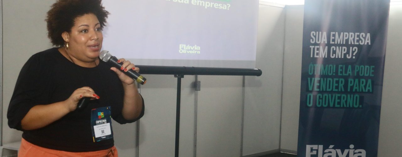 Palestra ‘Como Vender para o Governo’ destaca conhecimento e organização para vencer uma licitação pública #pracegover: Palestrante fala ao microfone; ao fundo telão com projeção do material da palestra